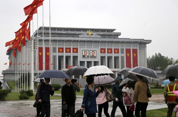 36년만에 열리는 북한 제7차 노동당 대회 개막일인 6일(현지시간) 대회장인 평양 4?25문화회관이 노동당기로 장식된 가운데 주민들이 우산을 들고 주위를 지나고 있다.  AP 연합뉴스