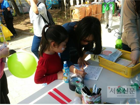 지난 어린이날 서울 금천구청에서 진행한 행사에서 한 여성이 아이와 함께 에코마일리지 가입 신청서를 쓰고 있다. 금천구 제공 