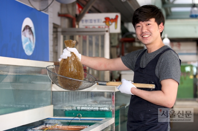서울 성동구 뚝도시장에 얼마 전 문을 연 뚝도수산 사장 김민우씨가 수족관의 활어를 들어보이며 웃고 있다. 