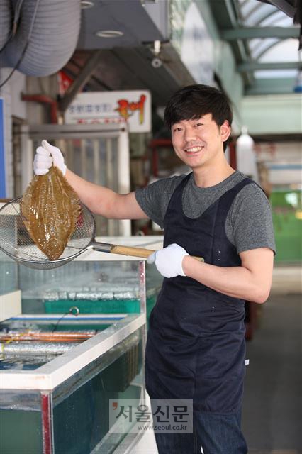 서울 성동구 뚝도시장에 얼마 전 문을 연 뚝도수산 사장 김민우씨가 수족관의 활어를 들어 보이며 웃고 있다.