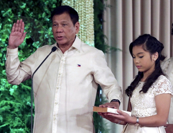 새로 선출된 로드리고 두테르테(왼쪽) 필리핀 대통령이 30일(현지시간) 마닐라 말라카낭 대통령궁에서 성경 위에 손을 얹고 취임 선서를 하고 있다. 오른쪽에 성경을 받치고 있는 사람은 그의 딸 베로니카다. 사진=EPA연합뉴스