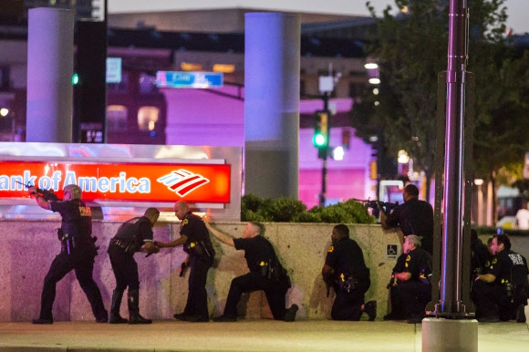 미국 텍사스주 댈러스 시내에서 벌어진 흑인 시위에 대응하던 경찰을 향한 조준 사격이 발생한 7일 밤(현지시간) 경찰들이 건물 벽에 바짝 붙어 저격범을 향해 총을 쏘며 움직임을 살펴보고 있다. 댈러스 AP 연합뉴스