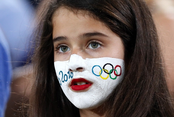 6일(현지시간) 브라질 리우데자네이루에서 열린 ‘2016 리우올림픽’ 테니스 여자 단식 비너스 윌리엄스(미국)와 커스텐 플립켄스(벨기에)의 경기장에 한 소녀가 얼굴에 오륜마크를 칠한 채 경기를 지켜보고 있다. AP 연합뉴스