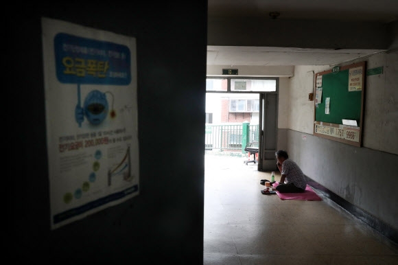 ‘전기요금 누진제’ 개편 논란이 일고 있는 10일 오후 서울 용산구의 한 아파트 입구 복도에 유철윤(71)씨가 자리를 깔고 앉아 있다.   유씨는 ”전기요금 누진제에 관한 뉴스를 봤다”며 ”전기세를 조금이라도 아끼려고 시원한 복도로 나왔다”고 말했다. 유례없는 폭염이 계속됨에도 불구하고 전기요금 누진제 적용으로 가정에서 전력 사용이 일정 수준을 넘어서면 ’요금 폭탄’을 맞을 수 있게 돼 서민들의 여름나기가 더욱 힘겨워질 것이라는 우려가 나온다.  연합뉴스