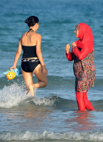 부르키니 차림의 한 무슬림 여성(오른쪽)이 지난 16일(현지시간) 튀니지 해변에서 더위를 식히면서 일반 수영복을 입고 지나가는 여성을 바라보고 있다. 가르엘멜 AFP 연합뉴스