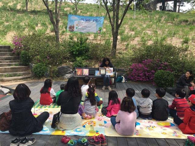 지난달 22일 서울 중랑구 능산공원에서 열린 힐링 독서체험 행사에서 어린이들이 자원봉사자의 설명을 들으며 함께 책을 읽고 있다. 중랑구 제공