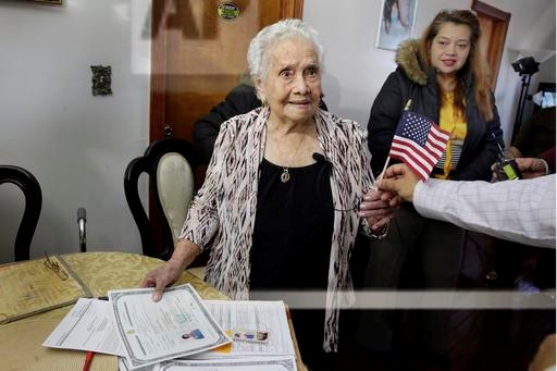 아메리카 마리아 에르난데스 할머니가 23일(현지시간) 뉴욕시 퀸즈의 자기 집 거실에서 귀화 증명서에 서명한뒤 딸(오른쪽)이 지켜보는 가운데 미국 국기를 받아들고 있다.  뉴욕 AP 연합뉴스