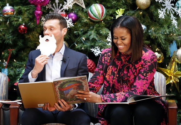12일(현지시간) 미국 워싱턴의 국립 아동 병원에서 열린 크리스마스 기념 이벤트에서 방송인 라이언 시크레스트(왼쪽)과 미셸 오바마 영부인이 책 ‘크리스마스 전날 밤’을 읽어주고 있다. AP 연합뉴스