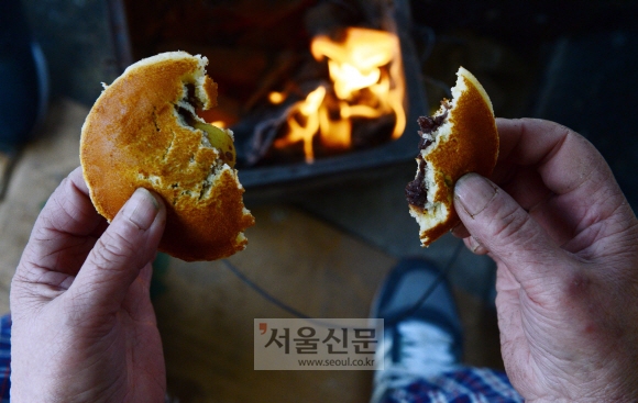 서울 중구 중림시장에서 생선을 파는 정정자(80) 할머니가 모닥불 위에서 손을 녹이며 빵 한 조각으로 점심 식사를 대신하고 있다.  정연호 기자 tpgod@seoul.co.kr