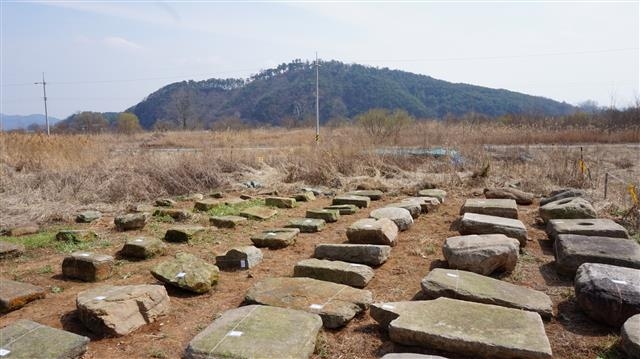 왕흥사 터에서 나온 석재와 강 건너 부소산의 모습. 왕흥사 터에 자리잡았던 10호 남짓한 민가는 절의 석재를 건축 자재로 쓰고 있었다. 발굴 조사와 함께 모두 수습해 한곳에 모아 놓았다.