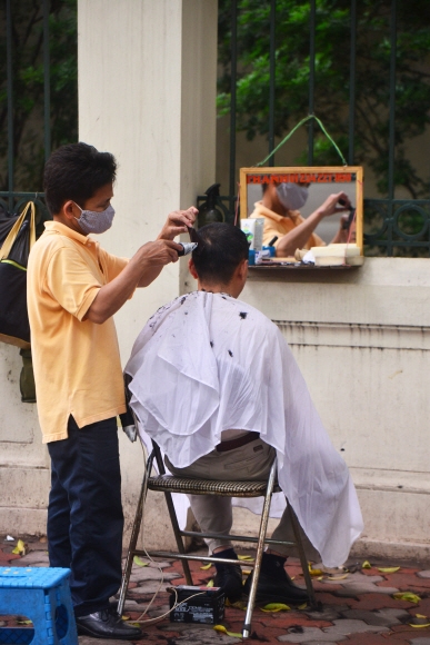 한 하노이 주민이 구시가의 건물 담벼락에서 머리를 깎고 있다.
