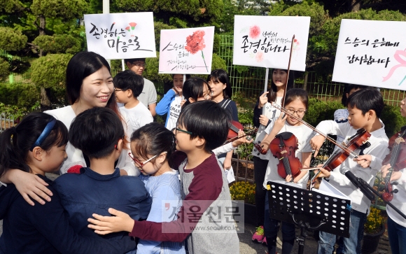 스승의 날인 15일 서울 송파구 풍성초등학교 학생들이 학교 교문에서 출근하는 교사에게 카네이션을 달아 주고 포옹하고 있다. 스승을 향한 존경심을 적은 손팻말과 ‘스승의 은혜’ 연주로 선물 대신 감사의 마음을 전했다. 박윤슬 기자 seul@seoul.co.kr