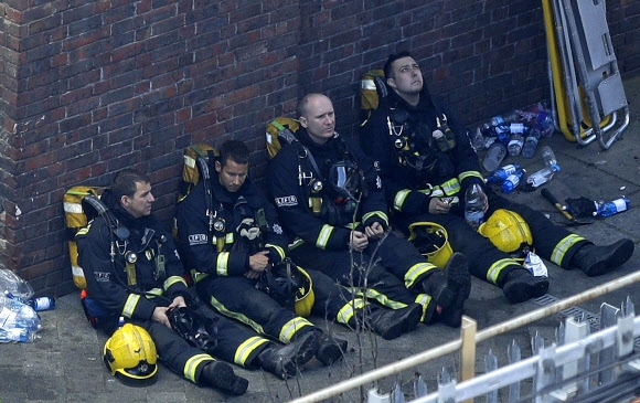 15일(현지시간) 그렌펠 타워 화재 진압 작업에 참여한 소방관들이 인근 건물 벽에 기댄 채 잠시 휴식을 취하고 있다. 런던 AP 연합뉴스