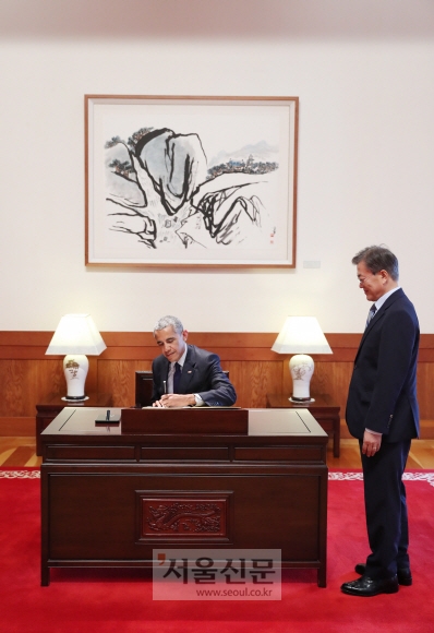 문재인 대통령이 3일 청와대에서 방한한 오마바 전 미대통령이 서명하는 모습을 지켜보고 있다.  청와대 제공