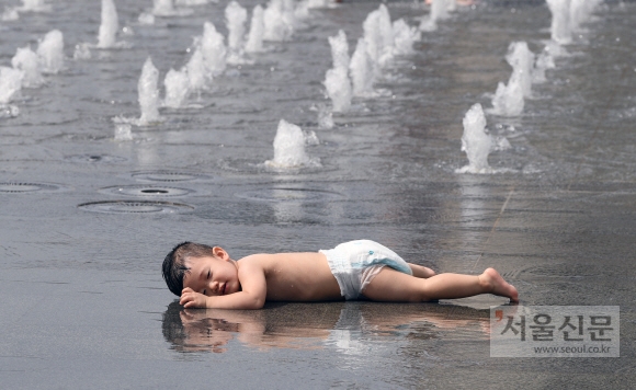 낮 최고기온이 34도까지 치솟은 19일 서울 광화문광장 분수대에서 한 어린아이가 흥건히 젖은 바닥에 엎드려 더위를 식히고 있다.  이호정 전문기자 hojeong@seoul.co.kr