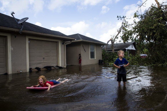 11일(현지시간) 미국 플로리다주 보니타 스프링스에 허리케인 어마가 휩쓸고 지나가 주택가로 물이 넘치자 천진난만한 아이들이 물놀이를 하고 있다. AP 연합뉴스