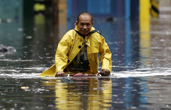 한 남성이 12일(현지시간) 필리핀 마닐라의 폭우로 물에 잠긴 거리에서 자전거를 타고 가고 있다. AP 연합뉴스