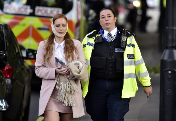 15일(현지시간) 영국 런던 남부 파슨스 그린 지하철역에 있던 지하철 객차에서 폭발로 추정되는 테러가 일어난 가운데 부상을 입은 여성이 경찰의 보호를 받으며 현장을 빠져 나오고 있다. AP 연합뉴스