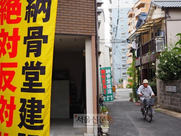 일본 오사카의 한 주택가에 납골당 건설 절대 반대 문구가 적힌 플래카드 옆을 한 주민이 자전거를 타고 지나가고 있다.