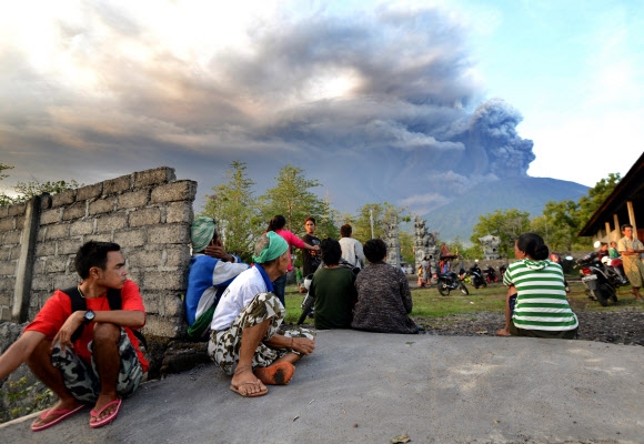 26일(현지시간) 인도네시아 발리 섬 아궁 화산이 분화해 화산재가 솟구치는 장면을 인근 마을 주민들이 지켜보고 있다. AFP 연합뉴스