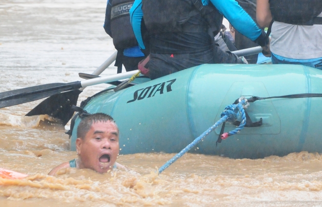 22일(현지시간) 필리핀 민다나오섬 카가얀데오로시에서 한 남성이 고무보트의 로프에 매달린 채 홍수가 발생한 지역에서 구조되고 있다. 로이터 연합뉴스
