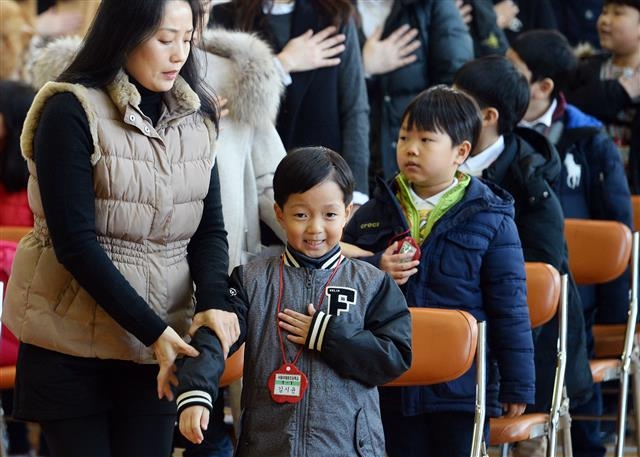 지난해 3월 서울 용산구 이태원초등학교에서 열린 입학식에서 한 학부모가 국기에 대한 경례를 하며 왼손을 가슴에 올린 자녀의 자세를 고쳐 주고 있는 모습.  서울신문 DB