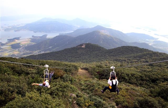 관광객이 금오산에 설치된 집와이어를 타고 시원하게 펼쳐진 다도해 바다를 보며 내려가고 있다.