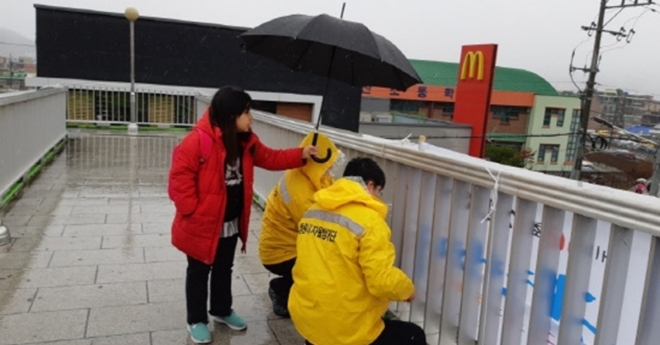 3월 21일 경남 창원 진해구 육교 위에서 현수막을 정비하던 자율방재단원의 모습을 보고 자신의 우산을 씌워준 어린이.  진해자율방재단