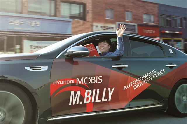 19일 충남 서산시 현대모비스 주행시험장에서 자율주행차 ‘엠빌리’를 테스트하는 연구원이 책을 보며 차창 밖으로 손을 흔들고 있다.  서산 연합뉴스