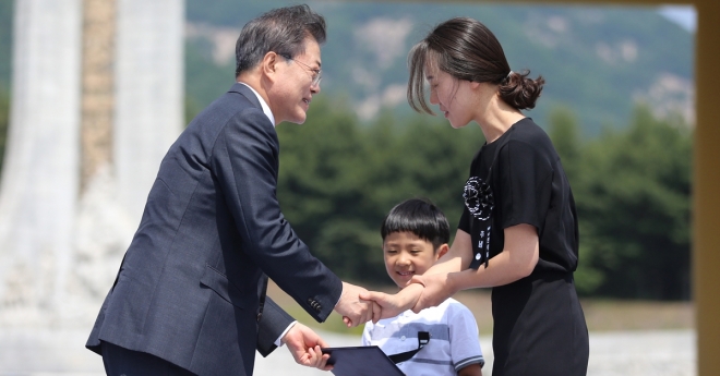 문재인(왼쪽) 대통령이 6일 오전 국립대전현충원에서 열린 제63회 현충일 추념식에서 한 시민의 생명을 구하다가 순직한 고 정연호 경위의 아들 정준용군에게 국가유공자 증서를 전달한 뒤 정 경위의 배우자 서지연씨와 악수하며 위로하고 있다. 2018.6.6 뉴스1. 국가보훈처 제공
