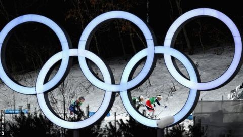 2018년 평창동계올림픽에 참여한 크로스컨트리 스키 선수들이 오륜 마크 뒤쪽에서 설원을 내달리고 있다. AFP 자료사진