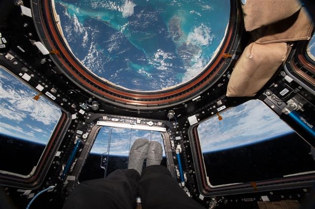 스콧 켈리가 ISS 내부에 있는 돔 형태의 쿠폴라에서 바하마 군도의 청록색 바다를 내려다보고 있다.  클 제공