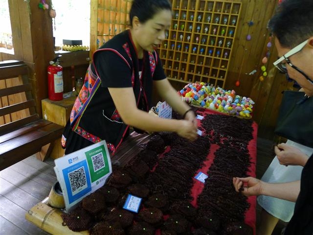 쉬솽반나의 원시삼림공원내 소수민족 마을에서 한 소수민족 판매원이 기념품을 모바일 결제를 통해 팔고 있다. 