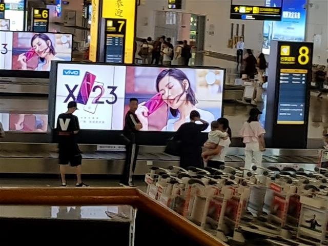 승객들이 광시성 난링 공항에서 대형 간판에 둘러싸여 수화물을 찾기 위해 기다리고 있다.