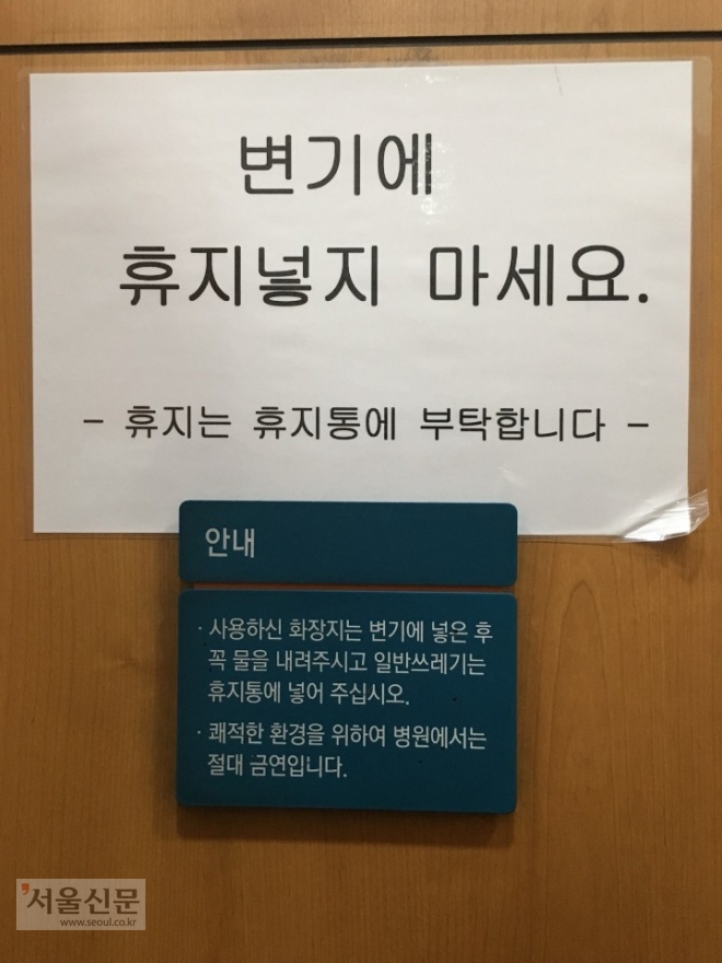 지난 9일 서울의 한 대형 병원 화장실에 써붙여진 안내문. A4 용지에는 “변기에 휴지넣지 마세요”라고 써있고, 바로 아래 안내문에는 “사용하신 화장지는 변기에 넣은 후 꼭 물을 내려달라”고 적혀 있다. 독자 제공