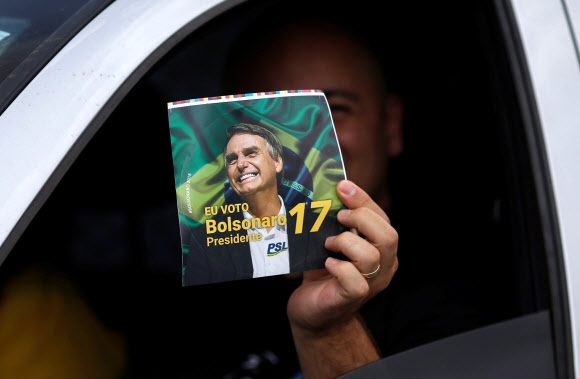 브라질 대통령 선거 결선투표를 하루 앞둔 27일(현지시간) 브라질리아에서 열린 사회자유당(PSL) 소속 자이르 보우소나루 대선 후보의 유세에 참가한 한 지지자가 그의 사진이 있는 선전물을 들어보이고 있다. 브라질리아 로이터 연합뉴스