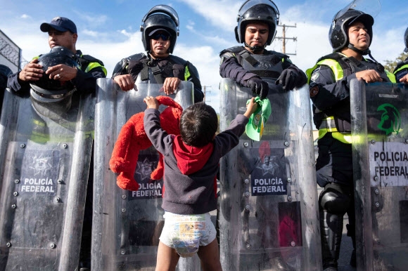 미국으로 이동하는 온두라스 출신의 중미 이민자의 어린아이가  22일(현지시간) 멕시코 바하 캘리포니아주 티후아나에 미국과 멕시코 국경에있는 El Chaparral 항구에서 멕시코 연방 경찰과 함께 놀고 있다. AFP 연합뉴스