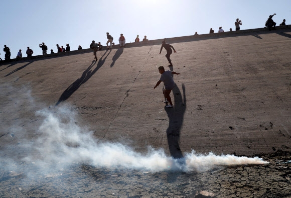 Migrants, part of a caravan of thousands traveling from Central America en route to the United States, run away from tear gas thrown by the U.S. border control near the border wall between the U.S and