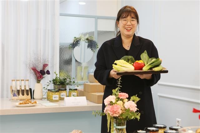 청년 창업의 꿈을 영글게 하는 서울 강동구의 ‘엔젤공방’ 사업을 통해 요리 교육·체험 공방 ‘잰아틀리에’(엔젤공방 12호)를 연 이재인 대표가 지난 6일 개소식에서 수업의 재료로 쓸 채소들을 한 아름 들고 환하게 웃고 있다.  강동구 제공