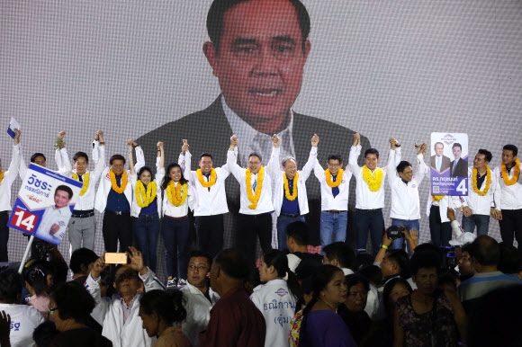 3·24 태국 총선이 초읽기에 들어간 가운데 집권 팔랑쁘라차랏당 후보들이 지난 15일 수도 방콕 퉁크루 거리의 한 유세장에서 쁘라윳 짠오차 총리의 대형 사진을 배경으로 손을 잡고 번쩍 치켜들면서 유권자들의 지지를 호소하고 있다. 방콕 EPA 연합뉴스