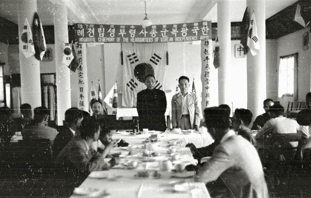 1940년 9월 중국 충칭 가릉빈관에서 한국광복군 총사령부 성립 전례식 뒤 열린 오찬 모습. 태극기를 배경으로 왼쪽에 서 있는 이가 김구다.  독립기념관 제공