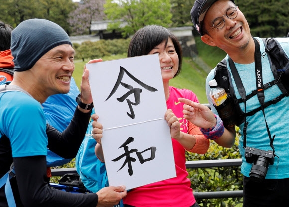 1일 일본 도쿄 고쿄(왕궁) 근처에서 나루히토 일왕의 도착을 기다리는 시민들이 이날부터 사용된 새 연호 ‘레이와’(令和)가 적힌 종이를 든 채 활짝 웃으며 기념촬영을 하고 있다.  도쿄 로이터 연합뉴스