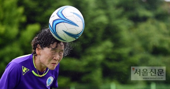 많은 비가 내리고 있는 가운데 펼쳐진 경기에서 동작여성축구단 유정규(64) 선수가 헤딩을 하자 얼굴에서 땀과 빗물이 흩어지고 있다.