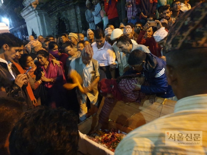 　Bandana Timalsina reaches out to touch her husband‘s face for the last time before his cremation at the Bagmati River. Kedar Timalsina committed suicide while working at a seafood factory in Busan, July 2019. The coffin carrying his dead body arrived at the Tribhuvan International Airport in Kathmandu on August 26.  [Ki Mindo/ The Seoul Shinmun]