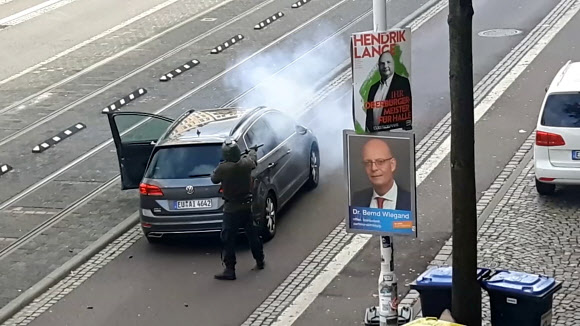 9일(현지시간) 독일 작센안할트주 할레에서 발생한 총격 사건의 용의자가 거리에 주차된 차량 뒤편에서 총기를 발사하고 있다. 할레 로이터 연합뉴스