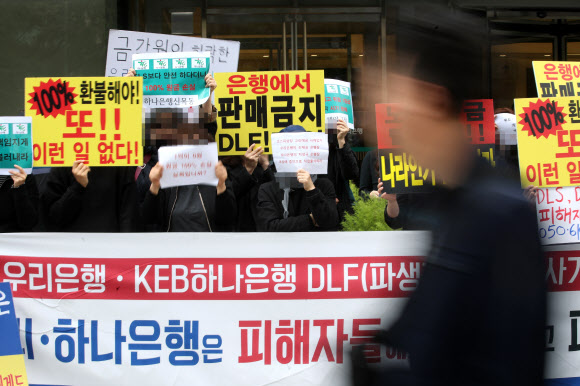 우리은행과 KEB하나은행이 판매한 해외 금리 연계 파생결합펀드(DLF)로 투자금을 잃은 피해자들이 지난 16일 서울 중구 KEB하나은행 앞에서 환불을 요구하는 손팻말을 들고 항의 집회를 벌이고 있다.  연합뉴스