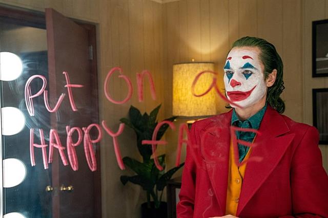 거울에 쓴 ‘Put on a happy face’( 행복한 얼굴을 만들어 봐 )란 글씨를 보고 있는 조커. 영화의 전반적인 주제가 담긴 문장이다.  워너브러더스코리아 제공