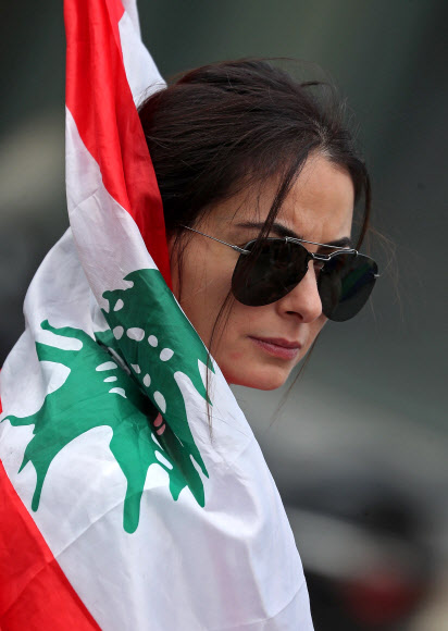 레바논 수도 베이루트에서 벌어진 13일째 반정부 시위에 참가한 한 여성이 29일(현지시간) 국기를 몸에 감고 생각에 잠긴듯 응시하고 있다. 베이루트 AFP연합뉴스