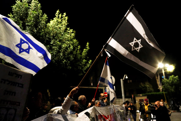 베냐민 네타냐후 총리에 반대하는 이들이 21(현지시간) 예루살렘에 있는 총리 관저 외부에서 이스라엘 국기를 들고 시위를 벌이고 있다. 예루살렘 로이터 연합뉴스