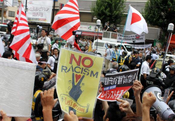 反人種差別市民は、日本の極右グループ、在日ザイニチの日本での特権を容認しない市民グループのメンバーの隣に反人種差別の看板を掲げます。市民グループは、行進中に昇る太陽の旗を掲げています。 日本では、 